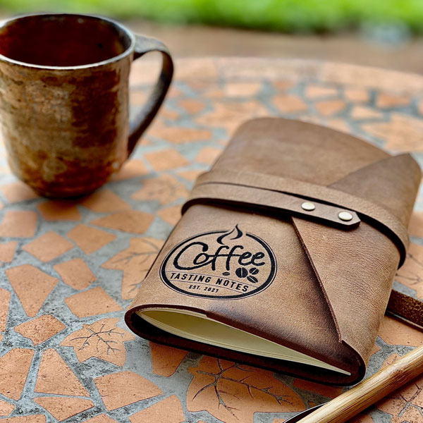 Leather personalised coffee tasting journal, wrap style, leather journal beside coffee atop table