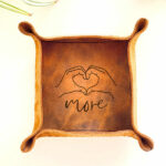 Small leather tray with an image of some hands in a heart shape and the word more engraved on the centre of the tray